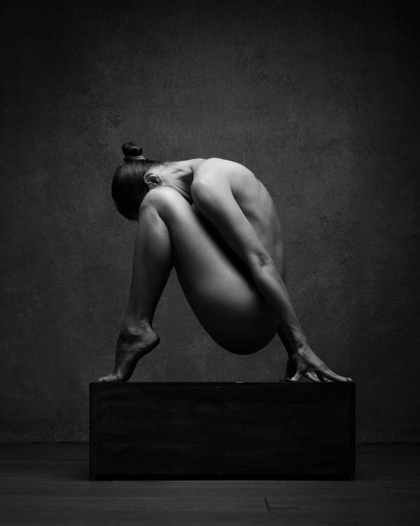 Woman crouched on a cube, head lowered, in stillness