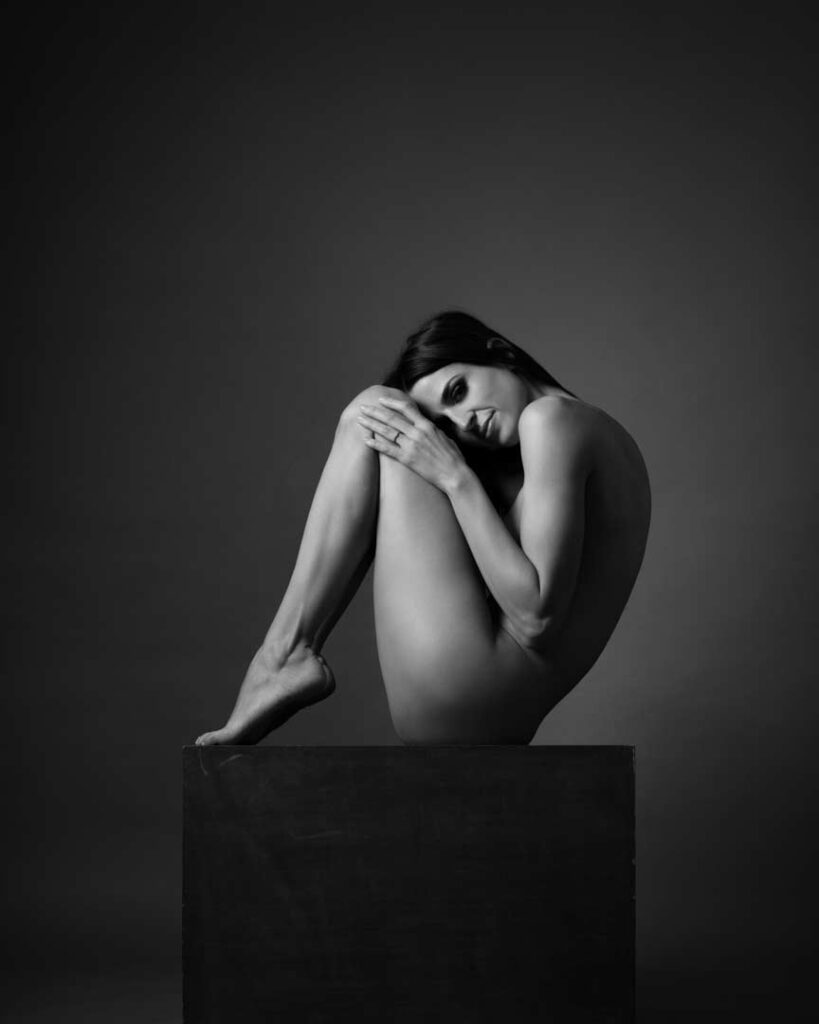 Nude woman curled up on a cube, resting her head gently