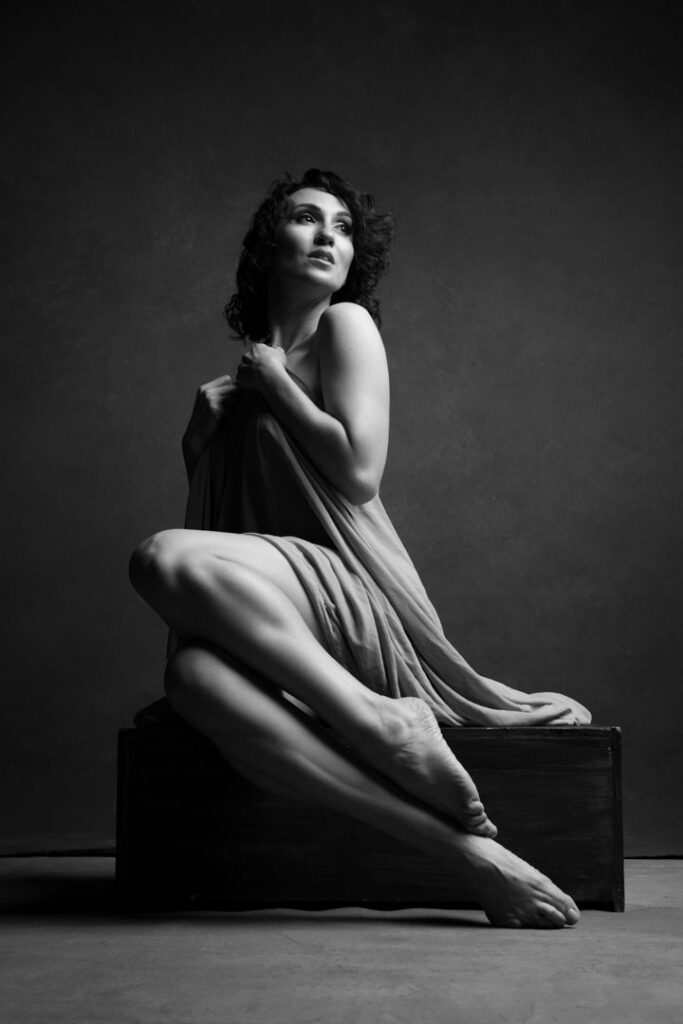 Seated woman wrapped in soft fabric, looking upward with elegance