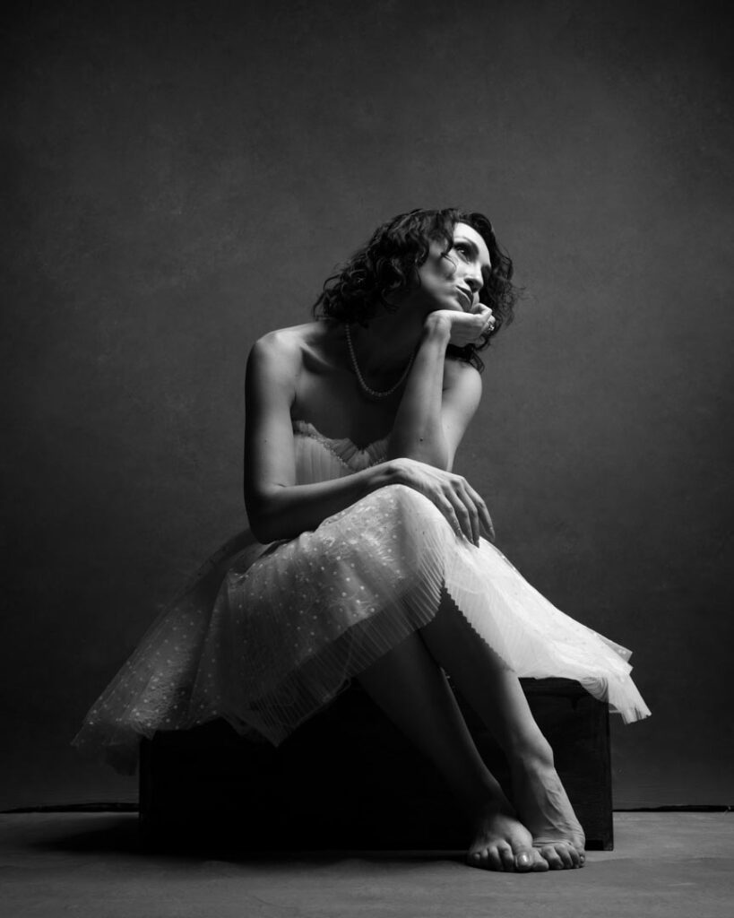 Woman seated under tulle fabric, backlit with softness