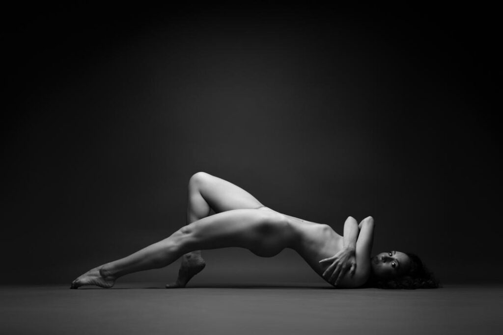 Nude artistic portrait of a woman lying down with elongated legs, in a sculptural black-and-white composition by Marco Barbera