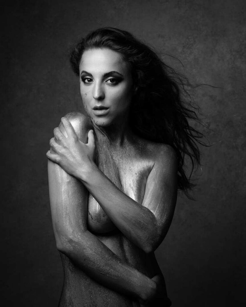Artistic black and white portrait of a topless woman with shimmering body paint, gazing directly into the camera. Photographed by Marco Barbera in Zürich