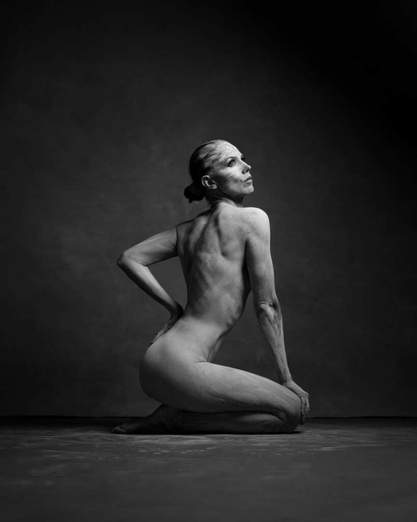 Fine art black and white portrait of a woman kneeling, her body painted with textured clay. Photography by Marco Barbera in Zürich.